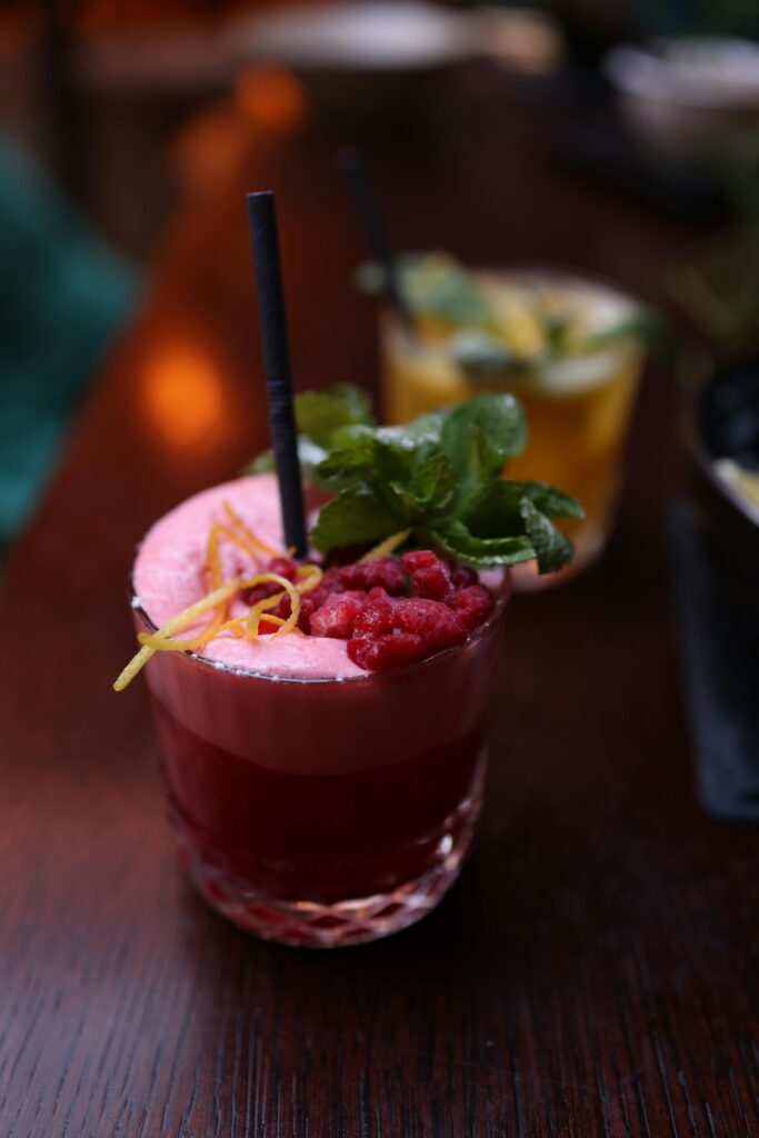 Vibrant raspberry cocktail with mint and lemon zest on wooden table.